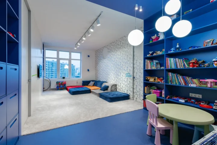 Boekenkast kinderkamer: blauwe kastenwand vol boeken en speelgoed in een ruime speelkamer