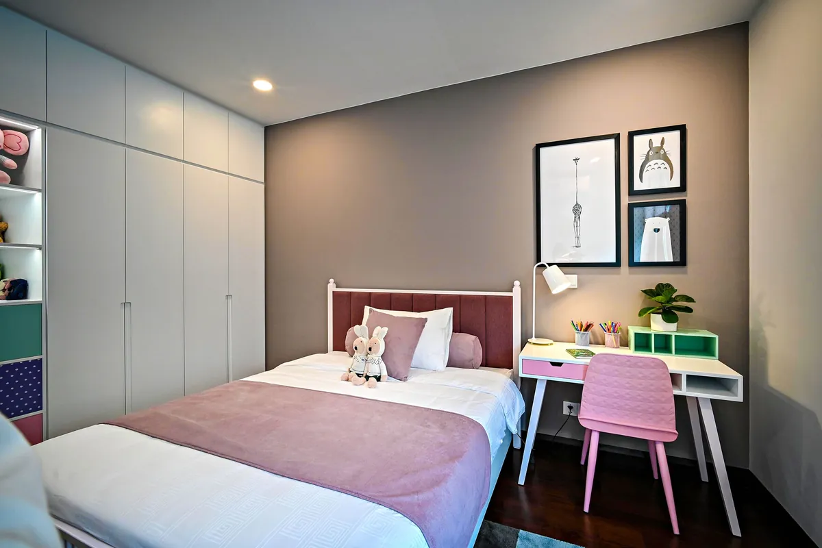 Witte kledingkast kinderkamer als kastenwand naast een kinderbed met roze dekbed en een klein bureau