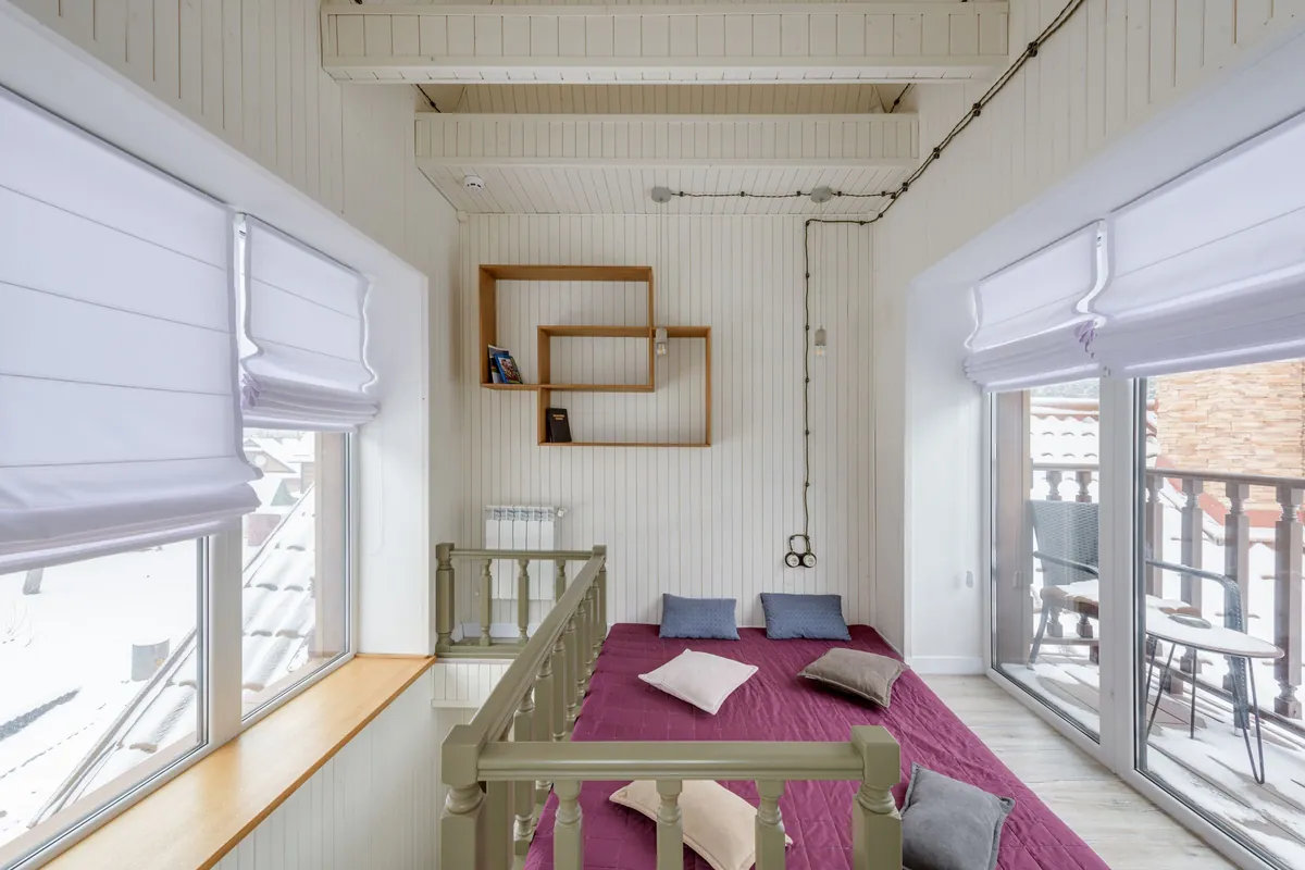 Kinderkamer op zolder met houten balken, breed bed, open wandplanken en grote ramen met vouwgordijnen