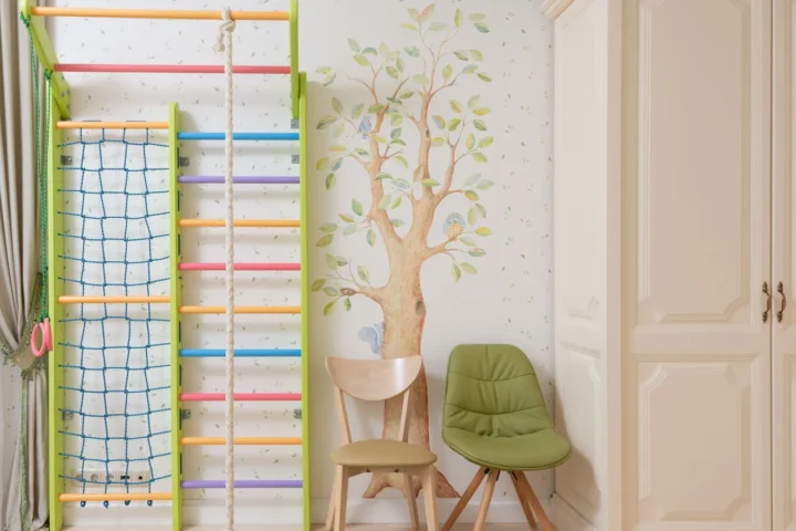 Crèmekleurige kledingkast in een kinderkamer met klimrek, groene stoel en boommuurschildering