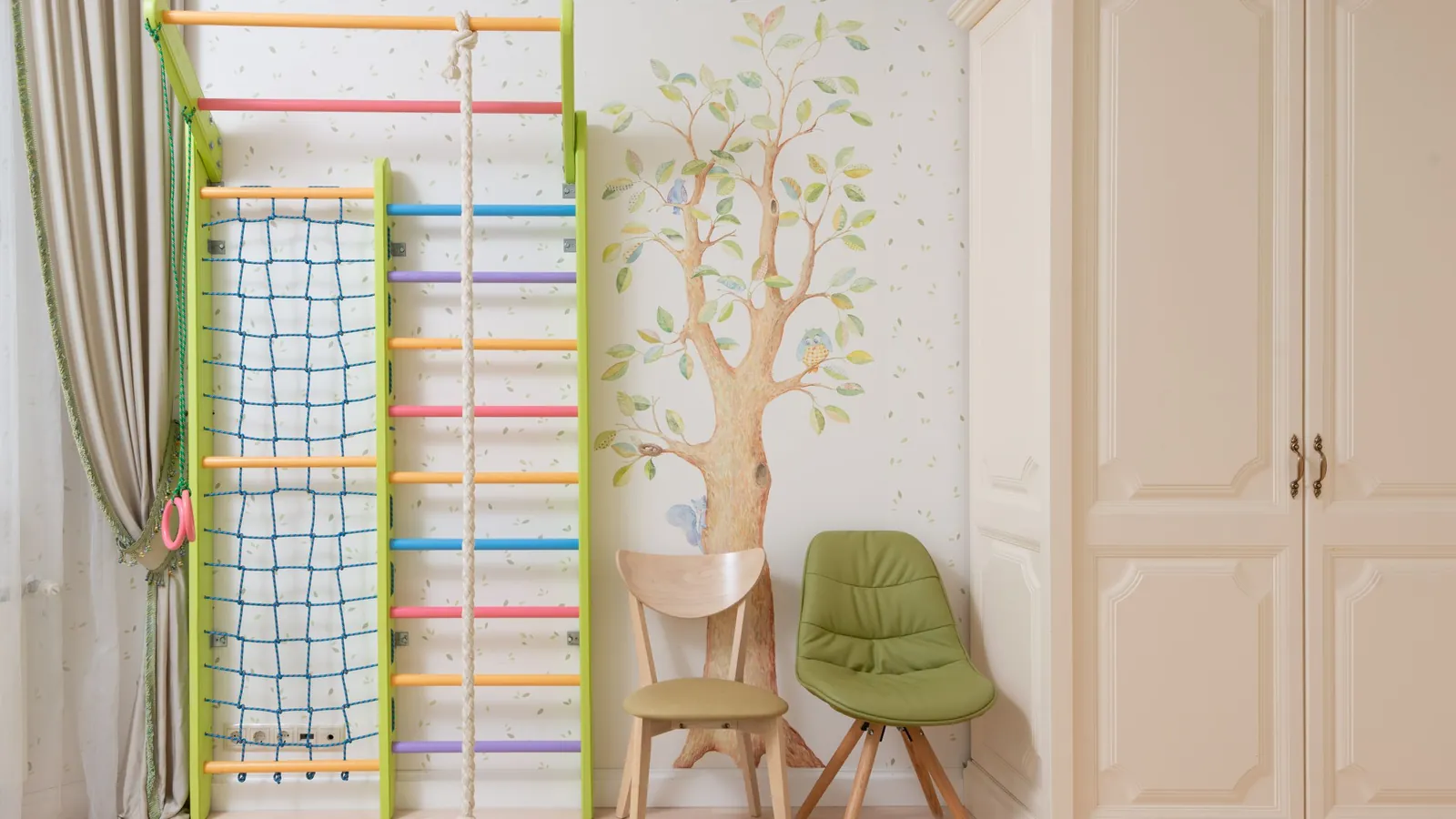 Crèmekleurige kledingkast in een kinderkamer met klimrek, groene stoel en boommuurschildering