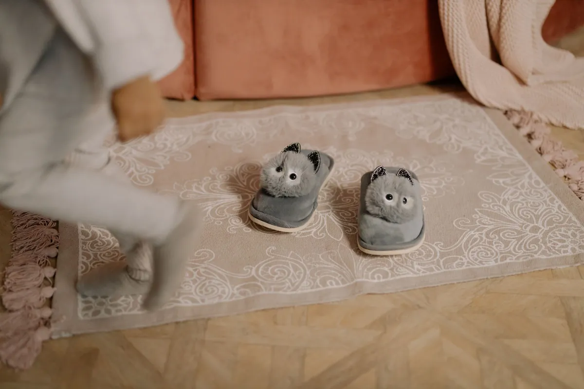 Lichtgrijs kleed met reliëfpatroon en kinderpantoffels op een visgraatvloer