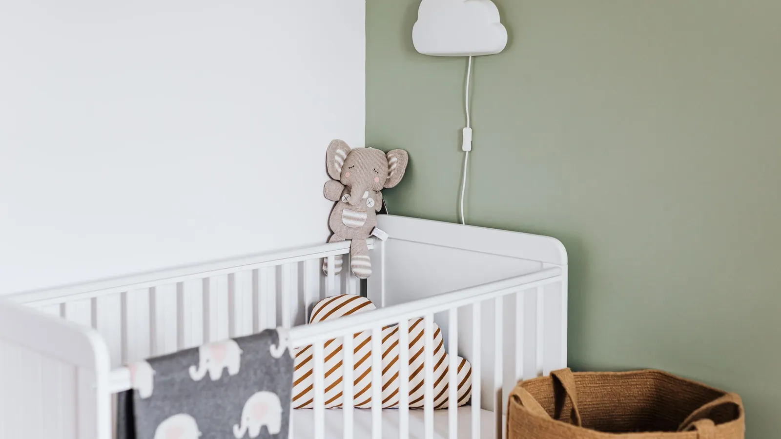 Lamp kinderkamer: wandlamp in de vorm van een wolkje boven een wit ledikant tegen een saliegroene muur