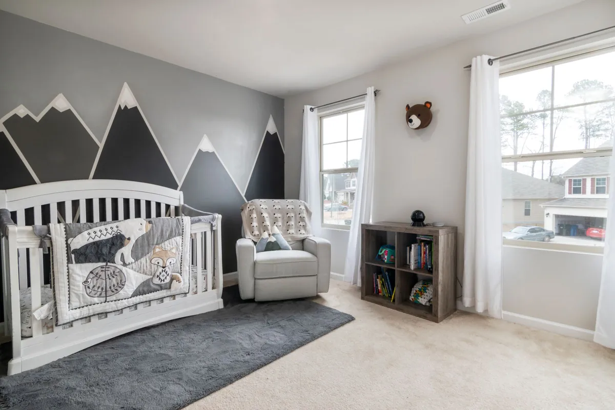 Babykamer met grijze en zwarte bergen als muurdecoratie boven een wit ledikant en een grijs vloerkleed