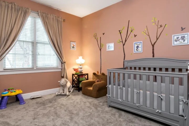 Muurstickers kinderkamer: boompjes en vogels op een oudroze muur in een babykamer met grijs ledikant
