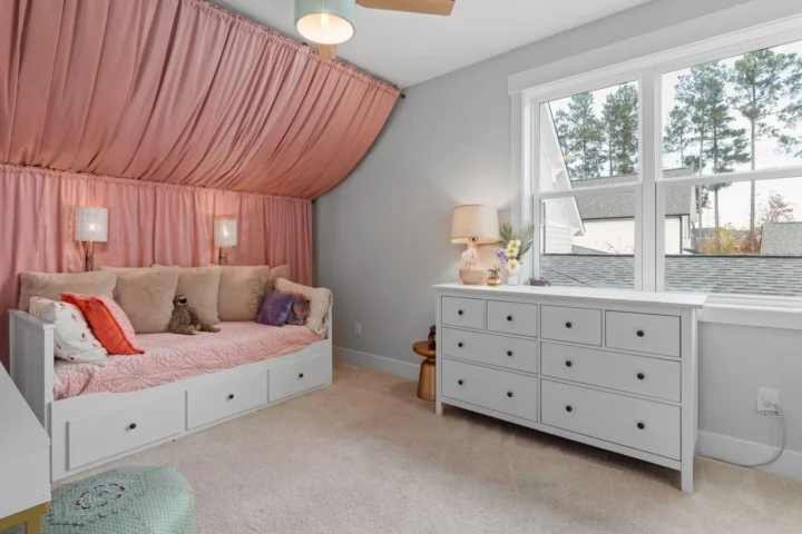 Oud roze kinderkamer met roze stof aan muur en schuin plafond, een witte bedbank en een witte ladekast