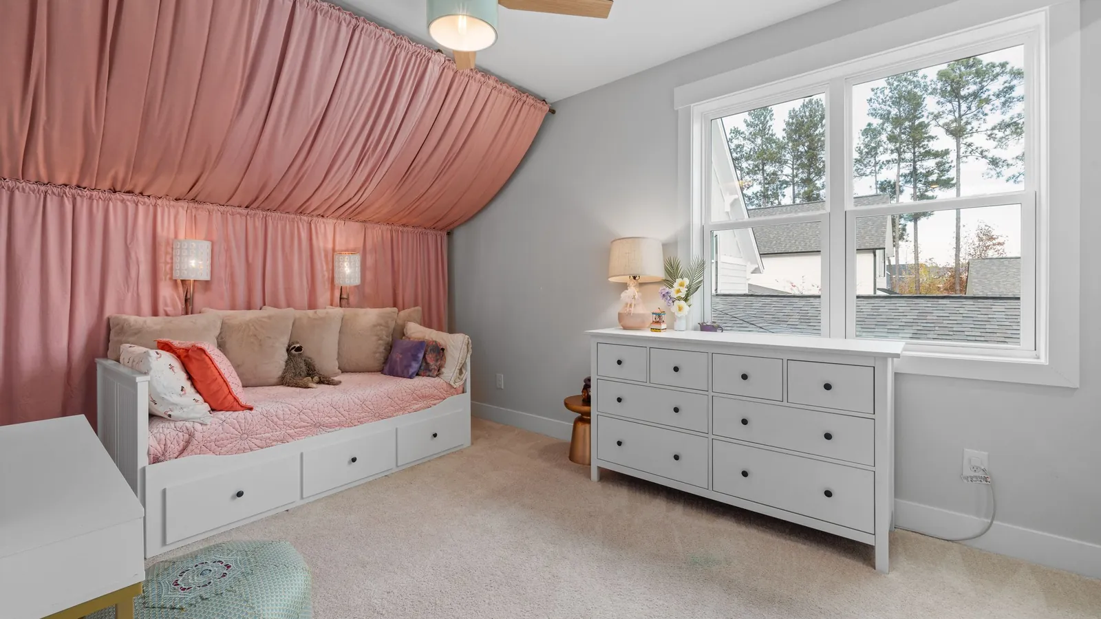 Oud roze kinderkamer met roze stof aan muur en schuin plafond, een witte bedbank en een witte ladekast
