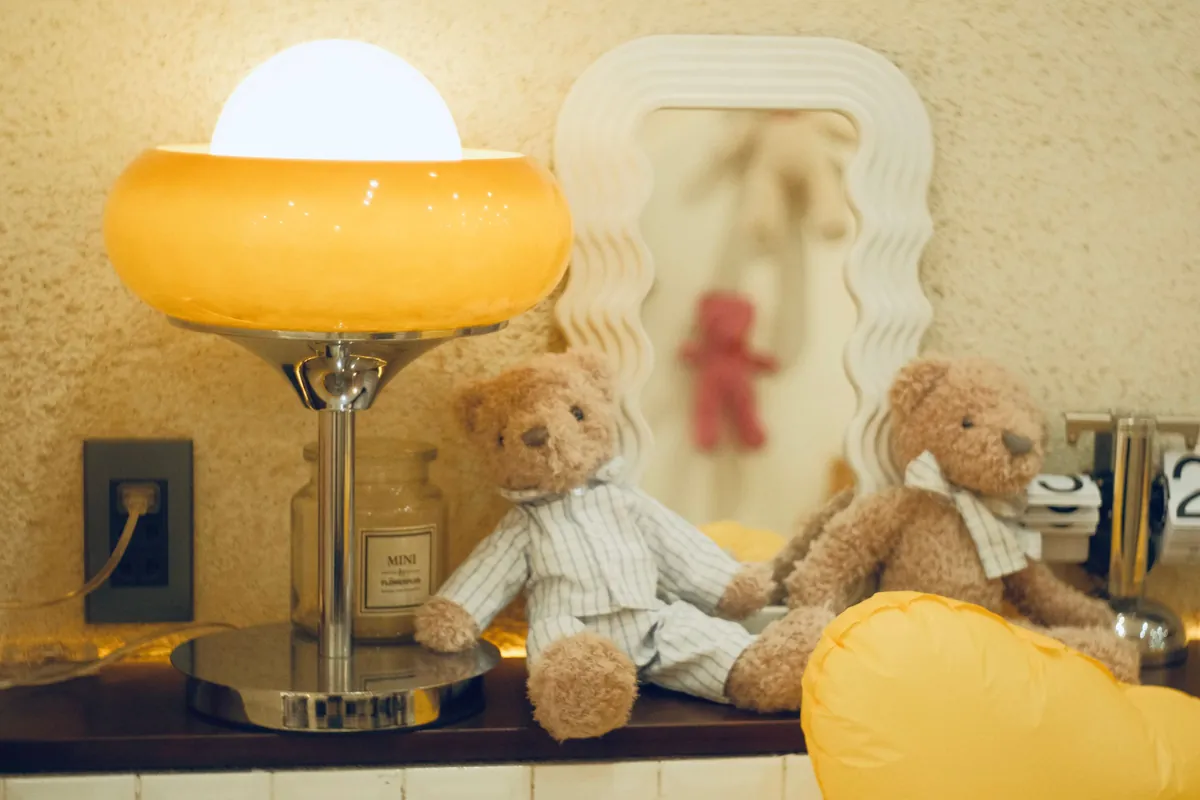 Tafellamp met warm licht naast twee knuffelberen op een plank in de kinderkamer