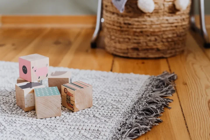 Vloerkleed kinderkamer: grijs geweven kleed met franjes en houten blokken op een houten vloer