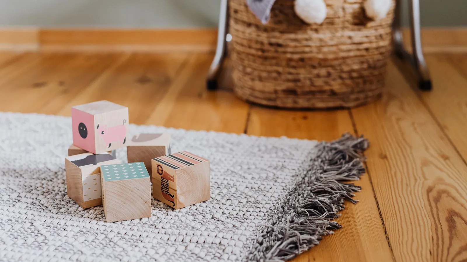 Vloerkleed kinderkamer: grijs geweven kleed met franjes en houten blokken op een houten vloer